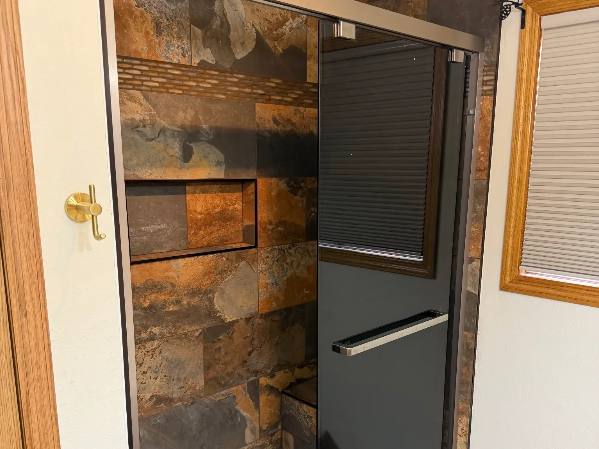 Walk-in shower with earth-tone tile, mosaic accent band, and glass door