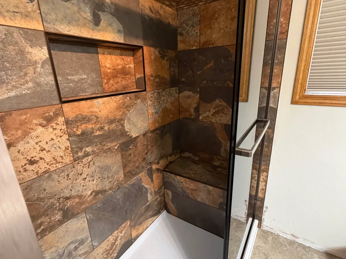 Walk-in shower interior with tiled niche, corner bench, and glass panel
