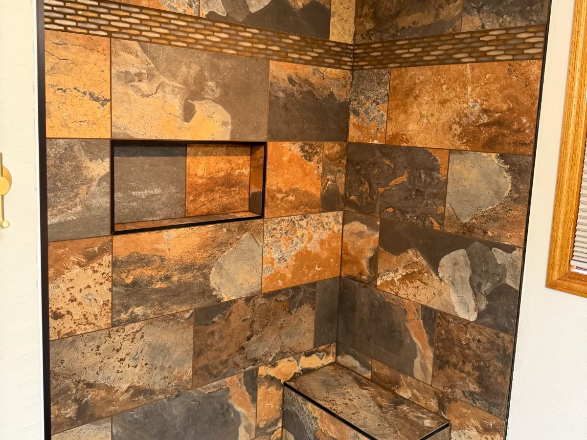 Detail of a tiled shower with accent band, niche, and corner bench
