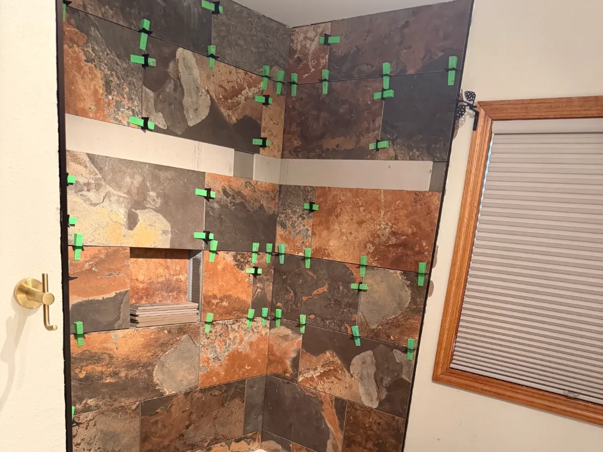 Shower wall tile being set with leveling clips during a bathroom remodel